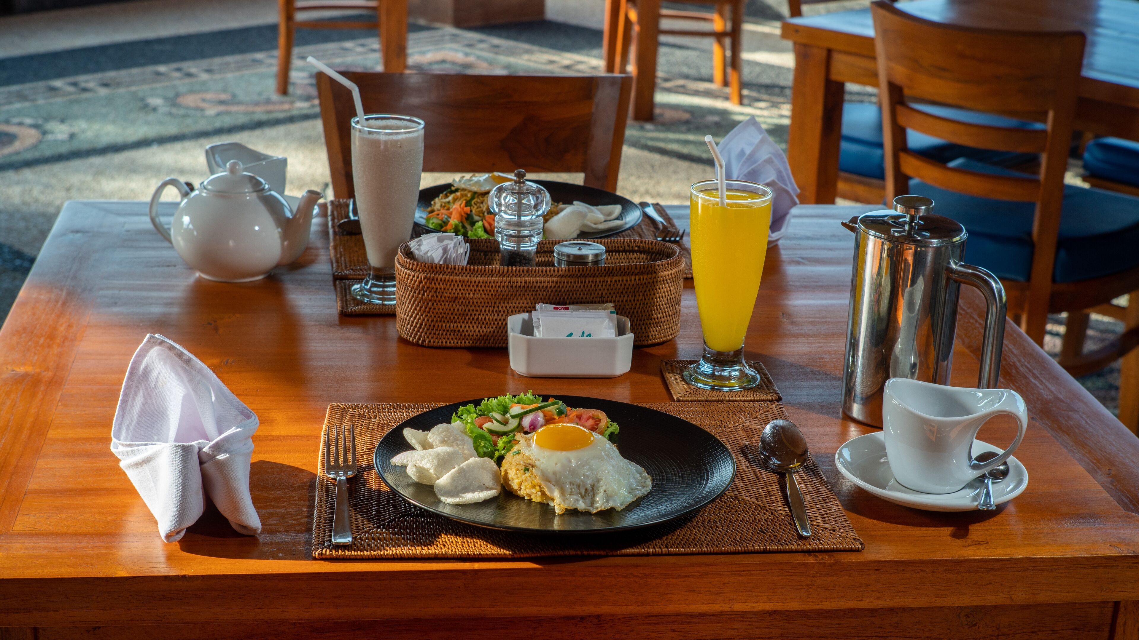 A breakfast table with a plate of food, a teapot, a glass of orange juice, and a coffee pot.
