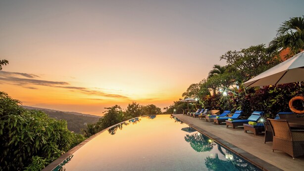 An infinity pool with a sunset view, lounge chairs, and umbrellas.
