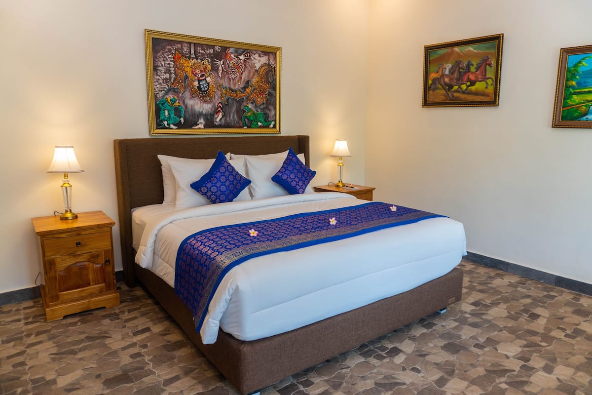 A neatly made bed with a blue and white bedspread, flanked by two nightstands with lamps, in a room with patterned flooring and two framed artworks on the wall.