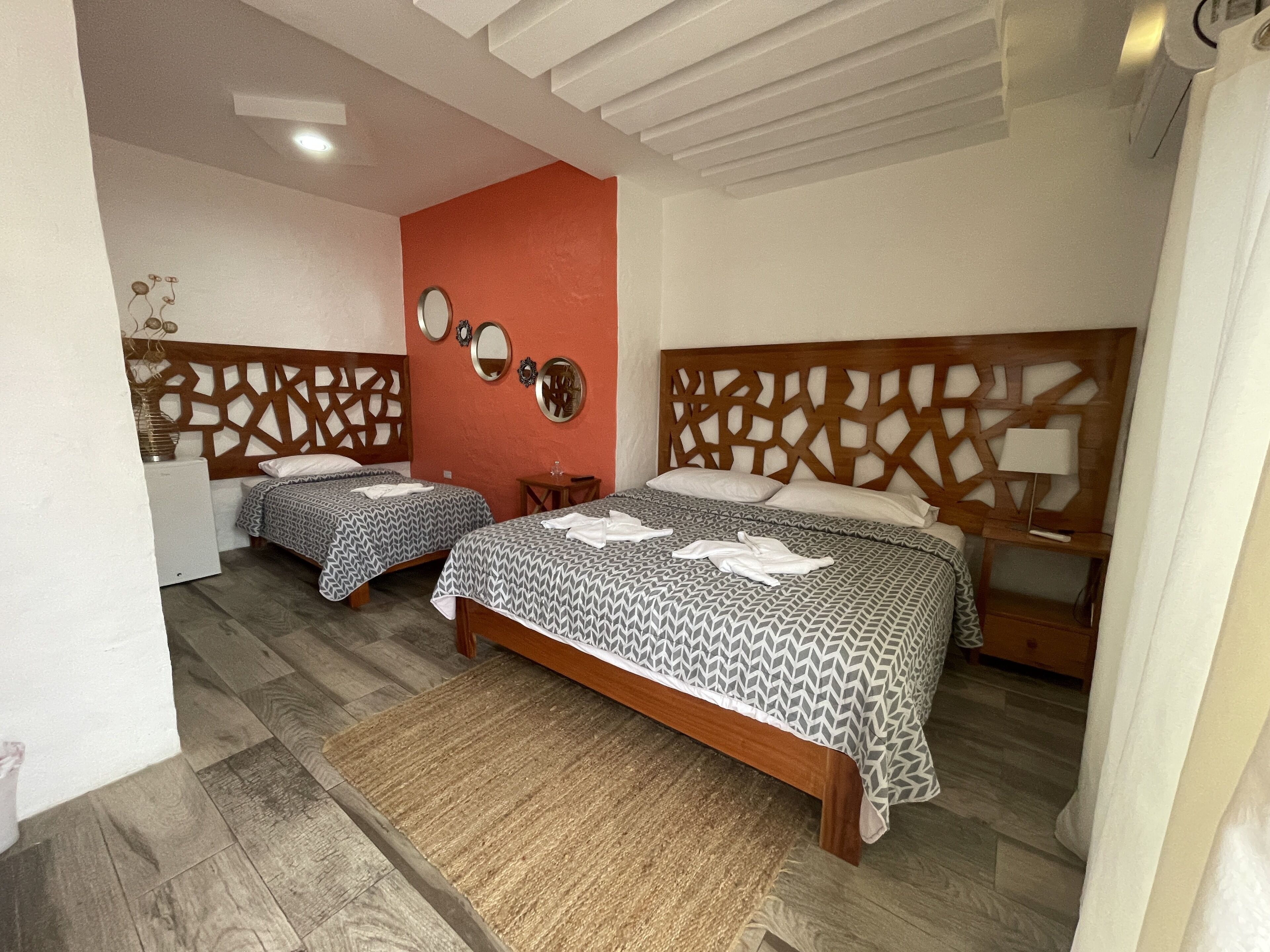 A hotel room with two beds, a wooden headboard, a small table, and a mirror on the wall.
