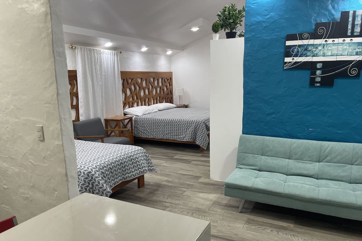 Una habitación moderna con dos camas, un sofá, una mesa y un elemento decorativo en la pared.