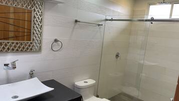 A modern bathroom with a glass-enclosed shower, a white sink, and a toilet.