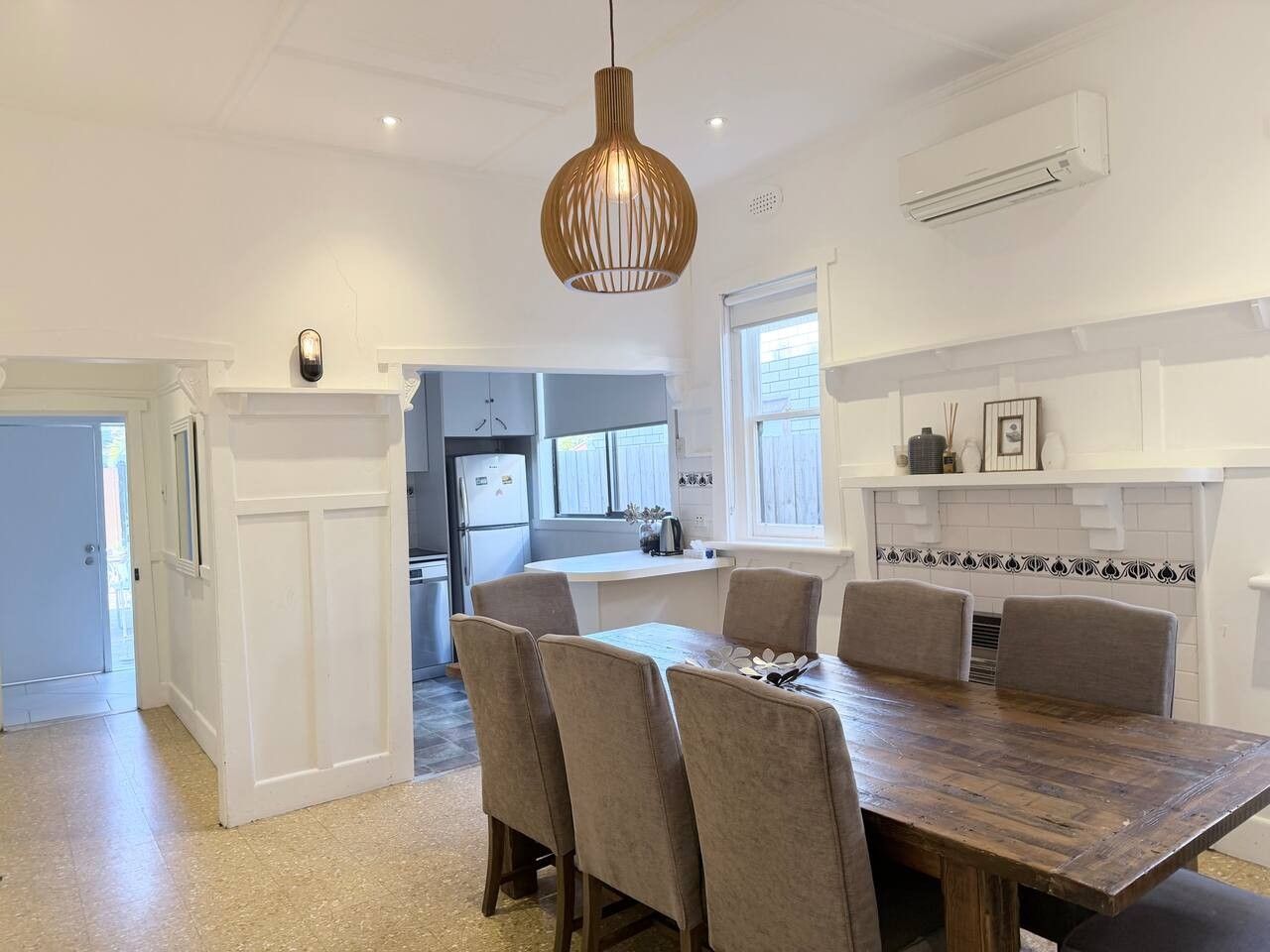 A modern kitchen with a dining area, featuring a wooden table, chairs, and pendant lighting.