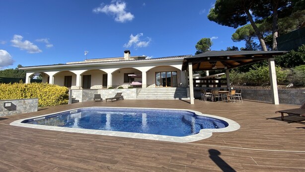 Una villa moderna con piscina, mobiliario de exterior y una pérgola.
