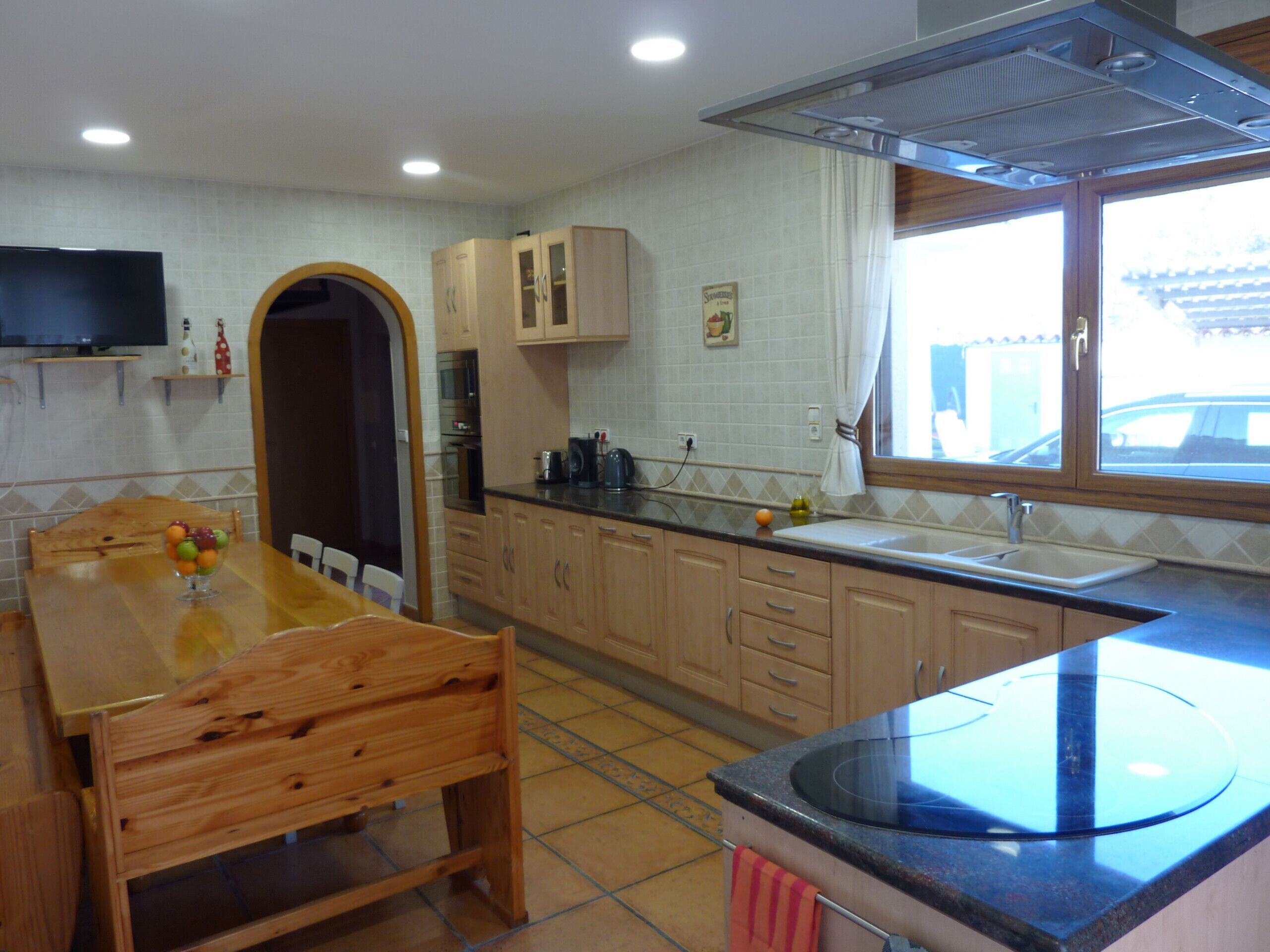 Een keuken met houten kastjes, een eettafel met stoelen, een inbouwoven en een raam met uitzicht.