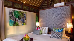 Habitación de hotel con cama, un cuadro de temática tropical, cabecera estampada y dos lámparas de noche.