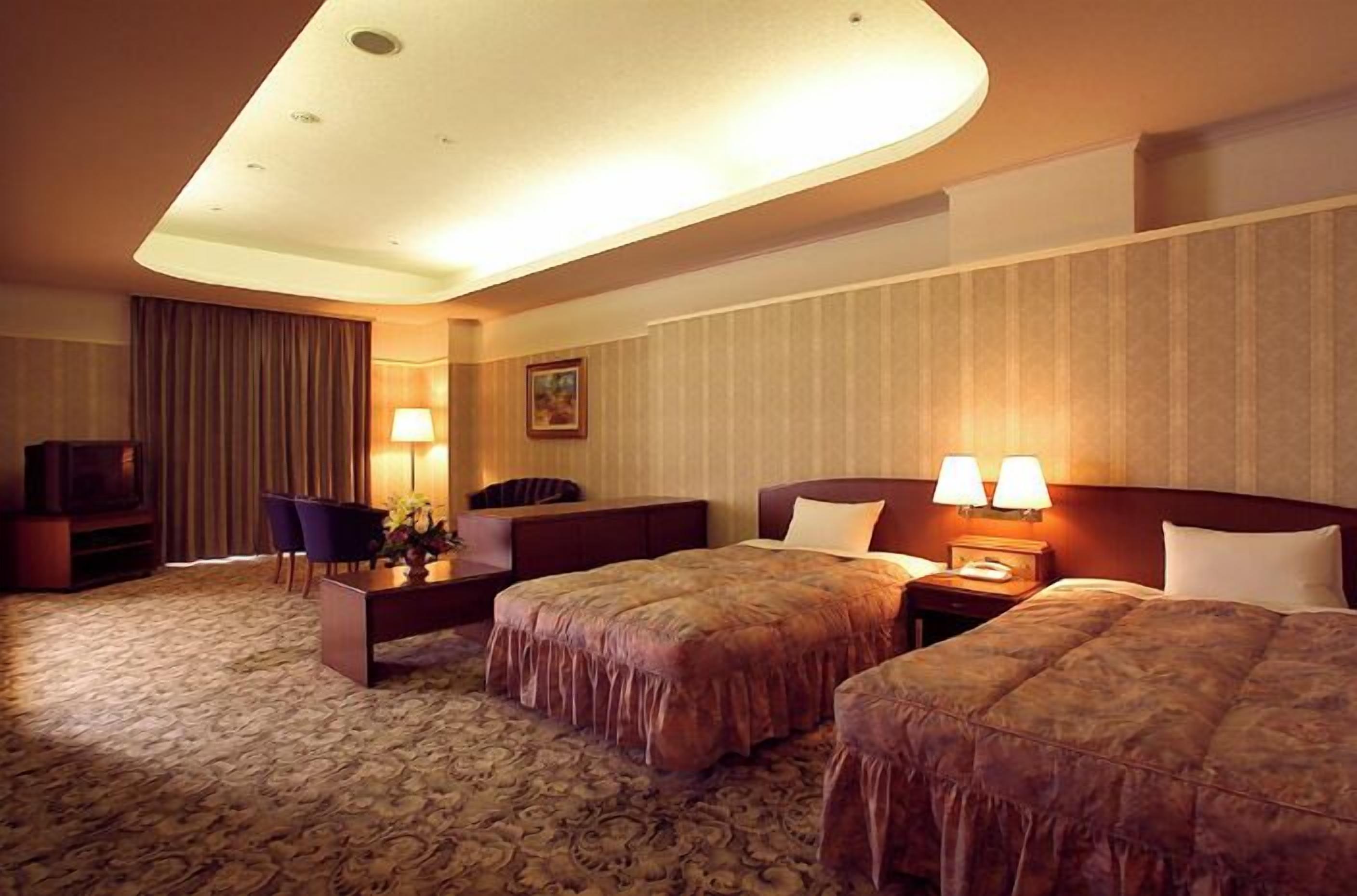 A hotel room with a curved ceiling, two beds, a desk, a chair, and a TV.