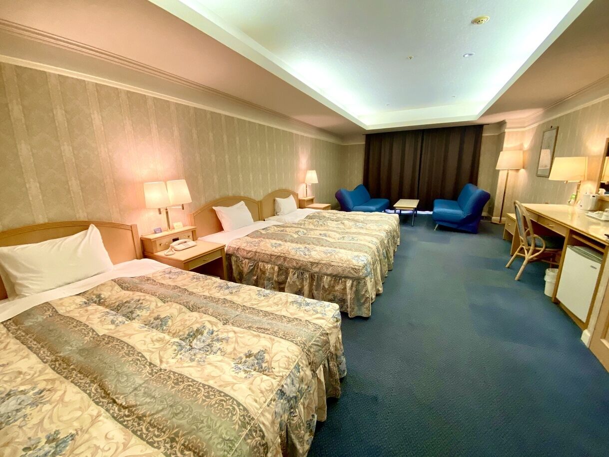A hotel room with three beds, a desk, a chair, and two lamps.