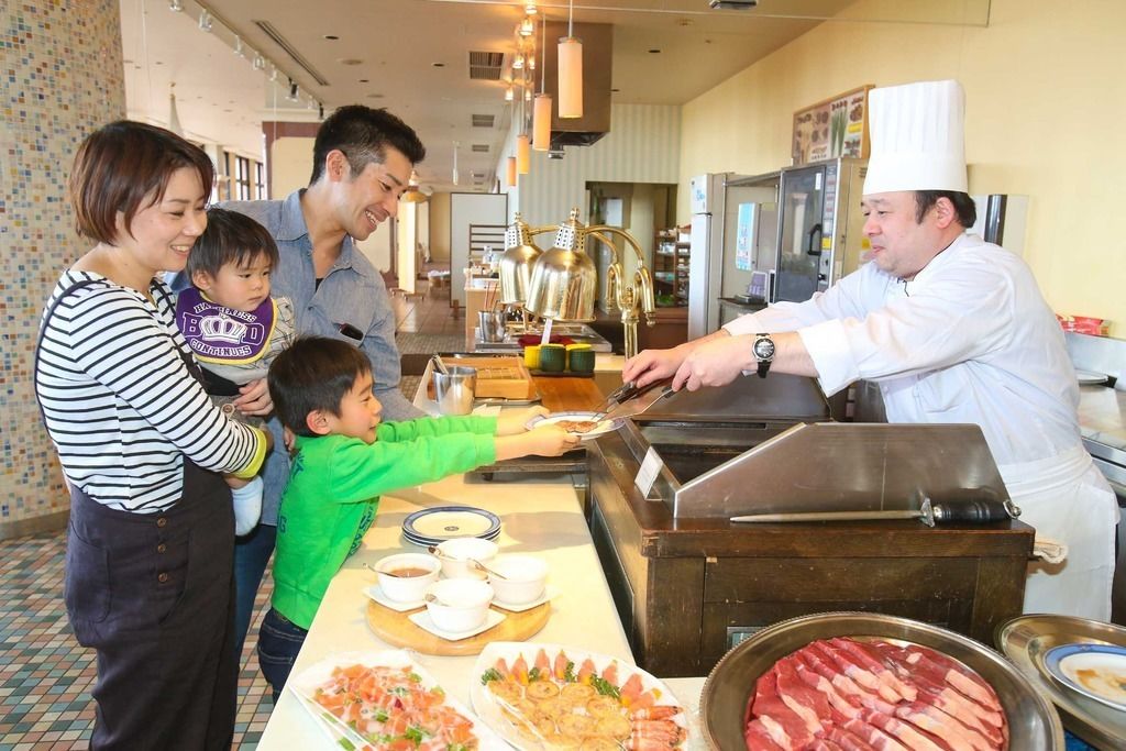 Een buffetopstelling met een kok die eten serveert, een gezin dat met elkaar omgaat en diverse gerechten die worden gepresenteerd.
