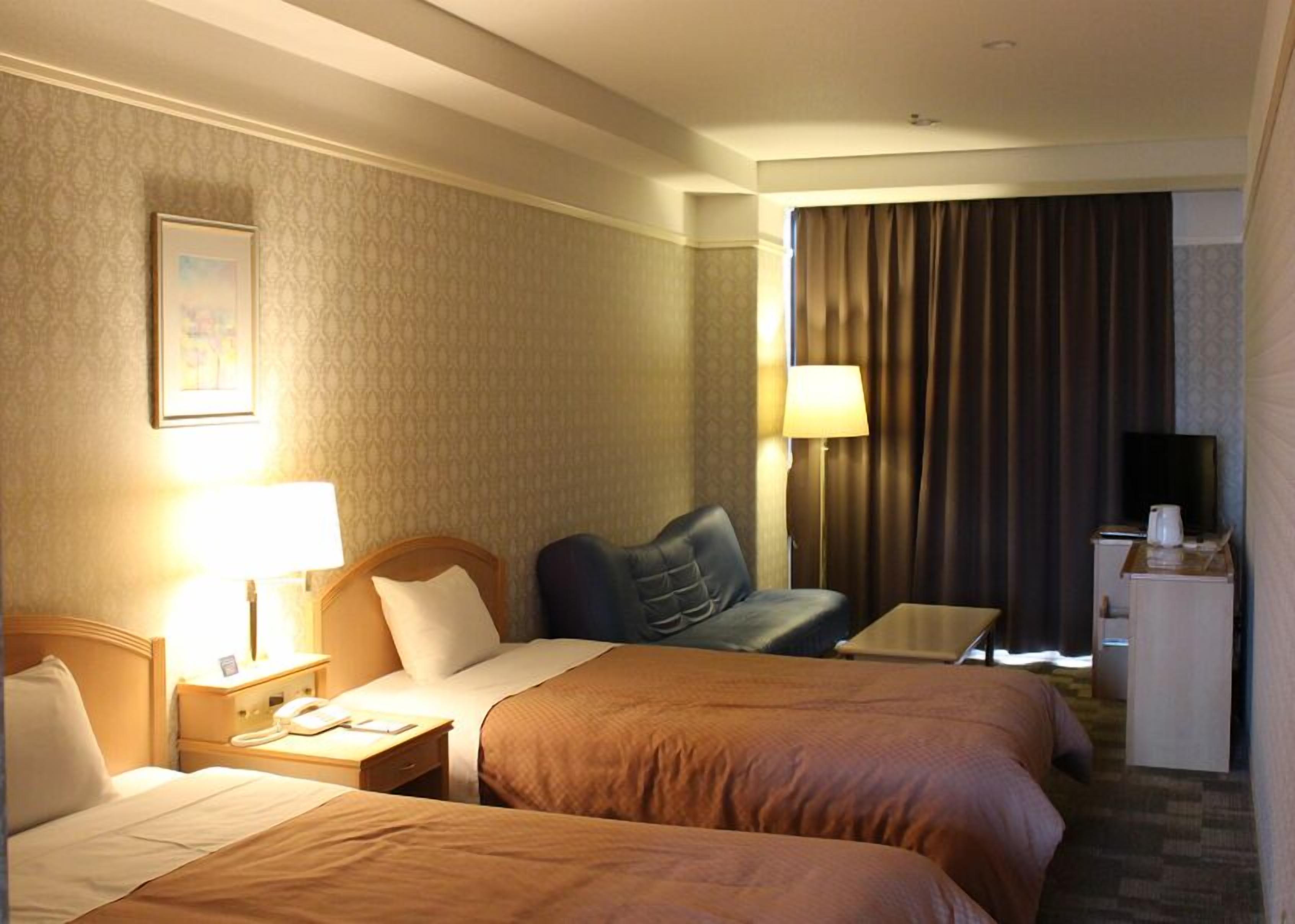 A hotel room with two beds, a desk, a TV, and a lamp.