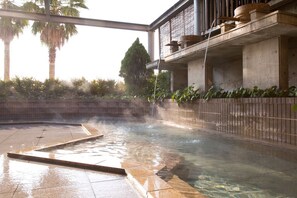 A hot spring area with a clear pool, a wooden deck, and a concrete structure with a water feature. - Hotel Sekia (Nankan)