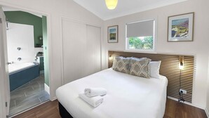 Une chambre à coucher avec un lit, une fenêtre, une porte et une salle de bain visible à travers une porte ouverte.