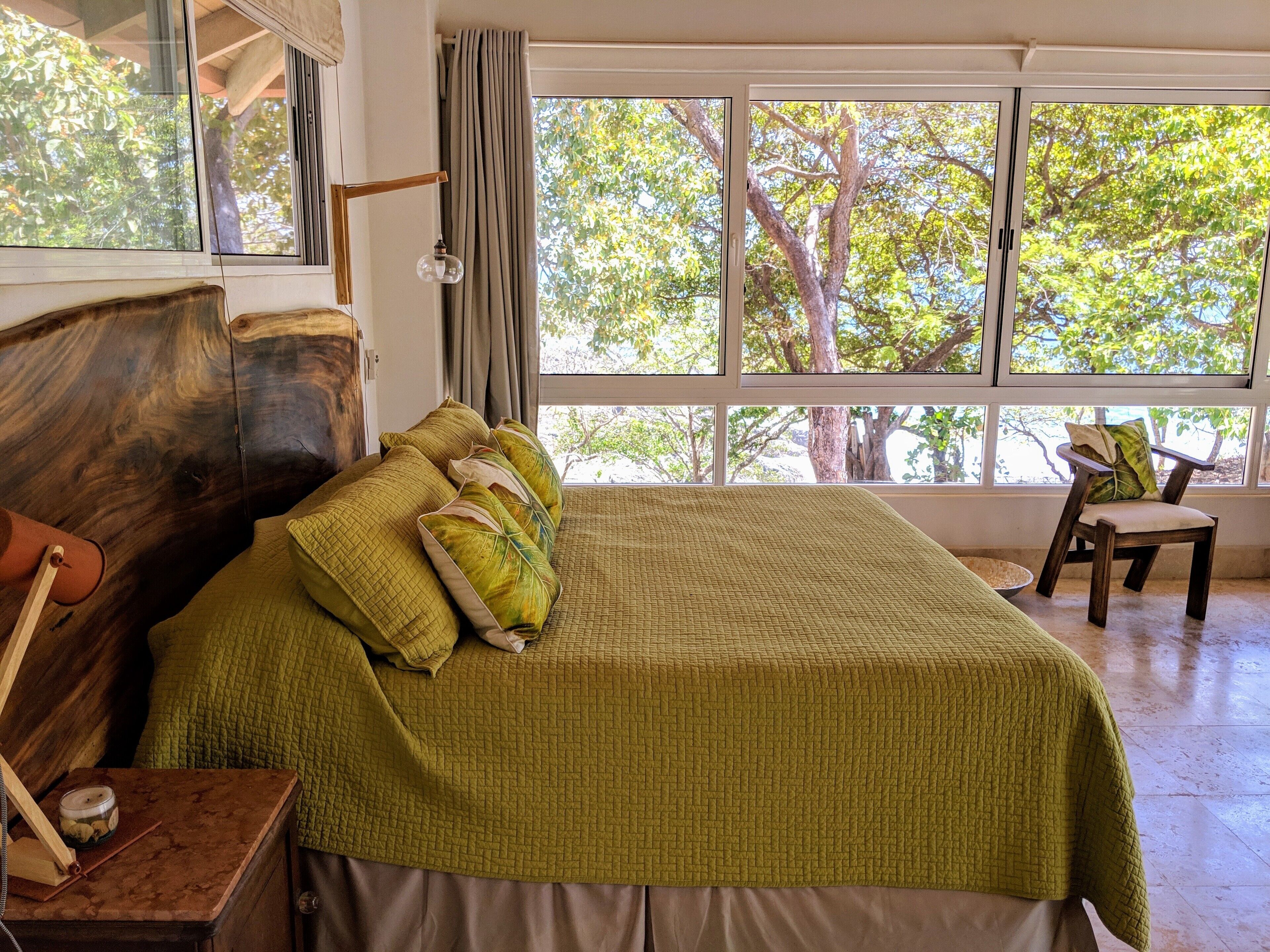 A bedroom with a large bed, a wooden headboard, and a view of trees through the window.
