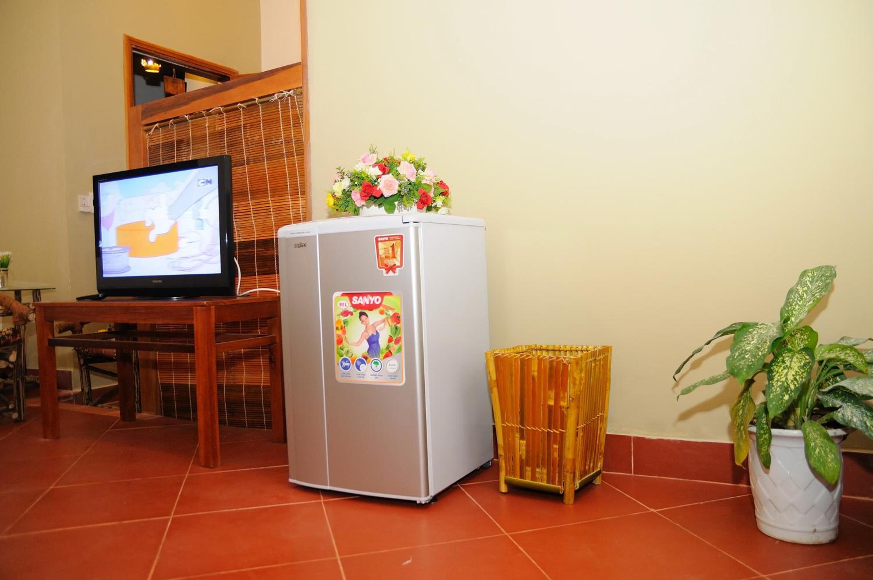 Ein gemütlicher Wohnbereich mit Fernseher, Kühlschrank, einem kleinen Tisch, einer Topfpflanze und einem Bambuskorb.