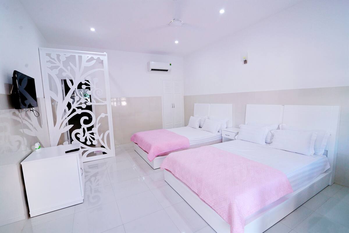 A hotel room with two beds, a white wardrobe, a small bedside table, and a decorative partition.