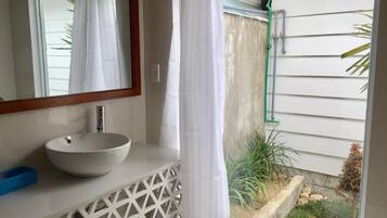A bathroom with a white sink, a mirror, and a window with a view of a garden.