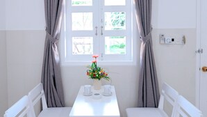 Una habitación con una mesa blanca y dos sillas blancas, una ventana con cortinas y una pequeña planta en maceta sobre la mesa.
