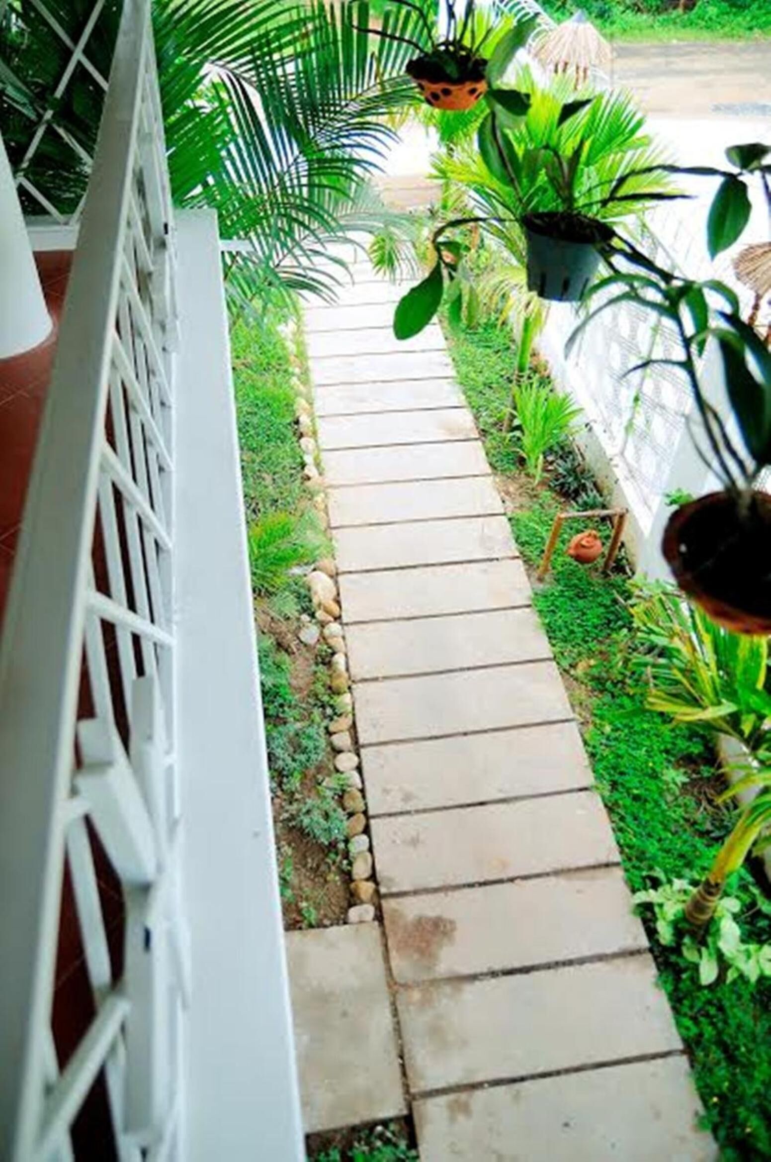 A pathway leading to a white fence with potted plants and a small garden area.