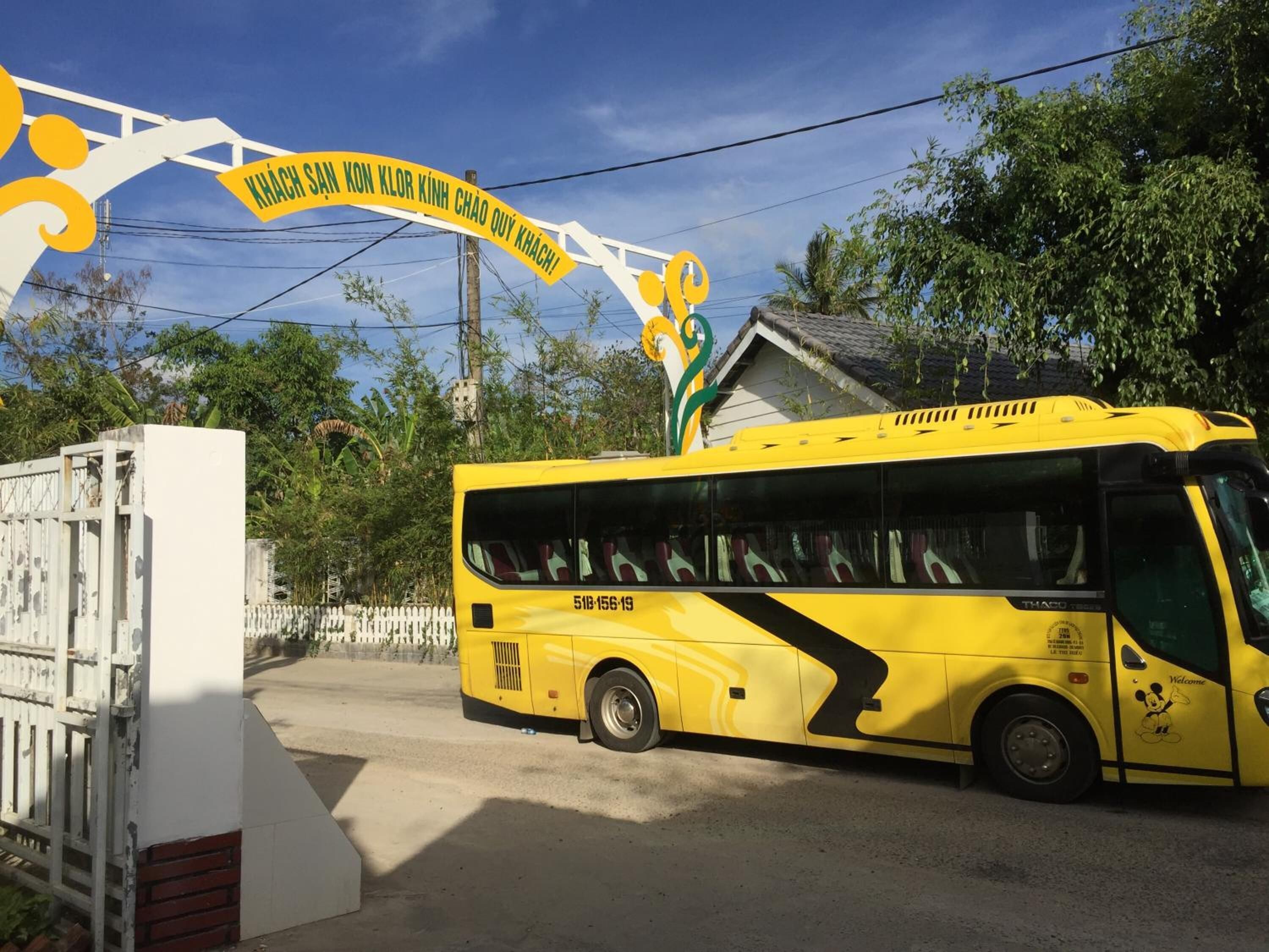 A yellow bus parked at a bus stop with a white fence and a building in the background.