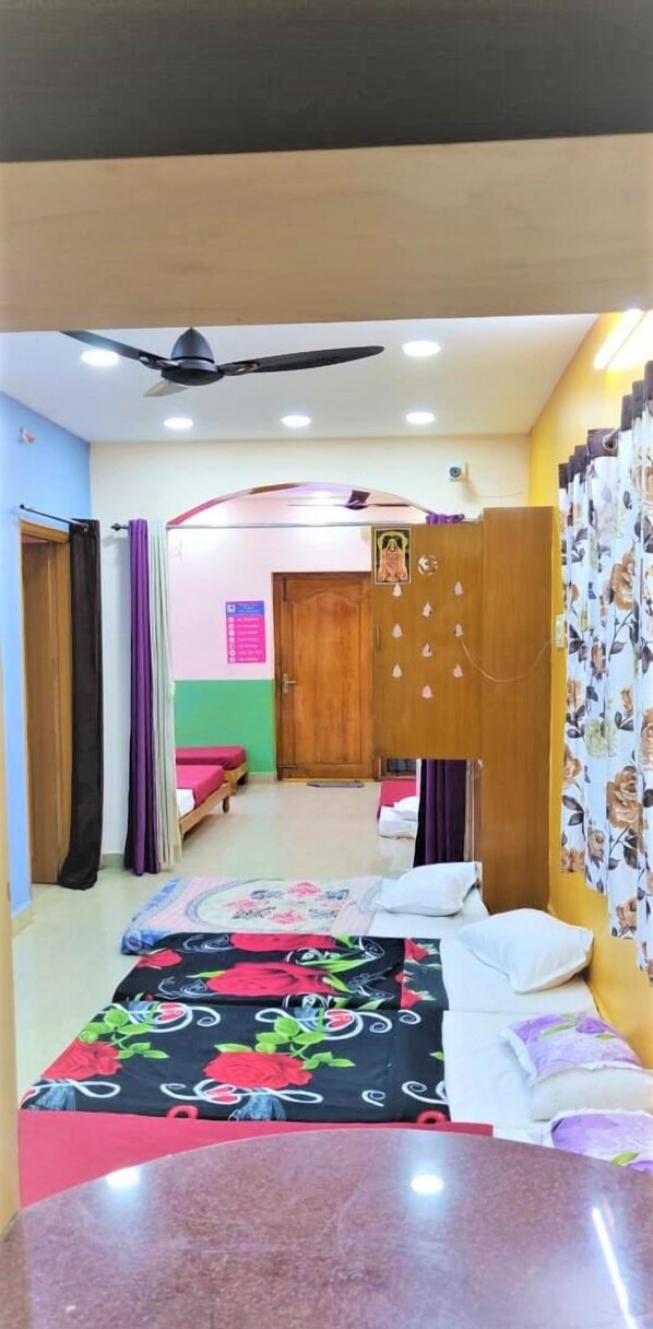 A bedroom with a bed, a wardrobe, a ceiling fan, and a door leading to another room. - Jayaram Residency Tirupathi (Tirupati)