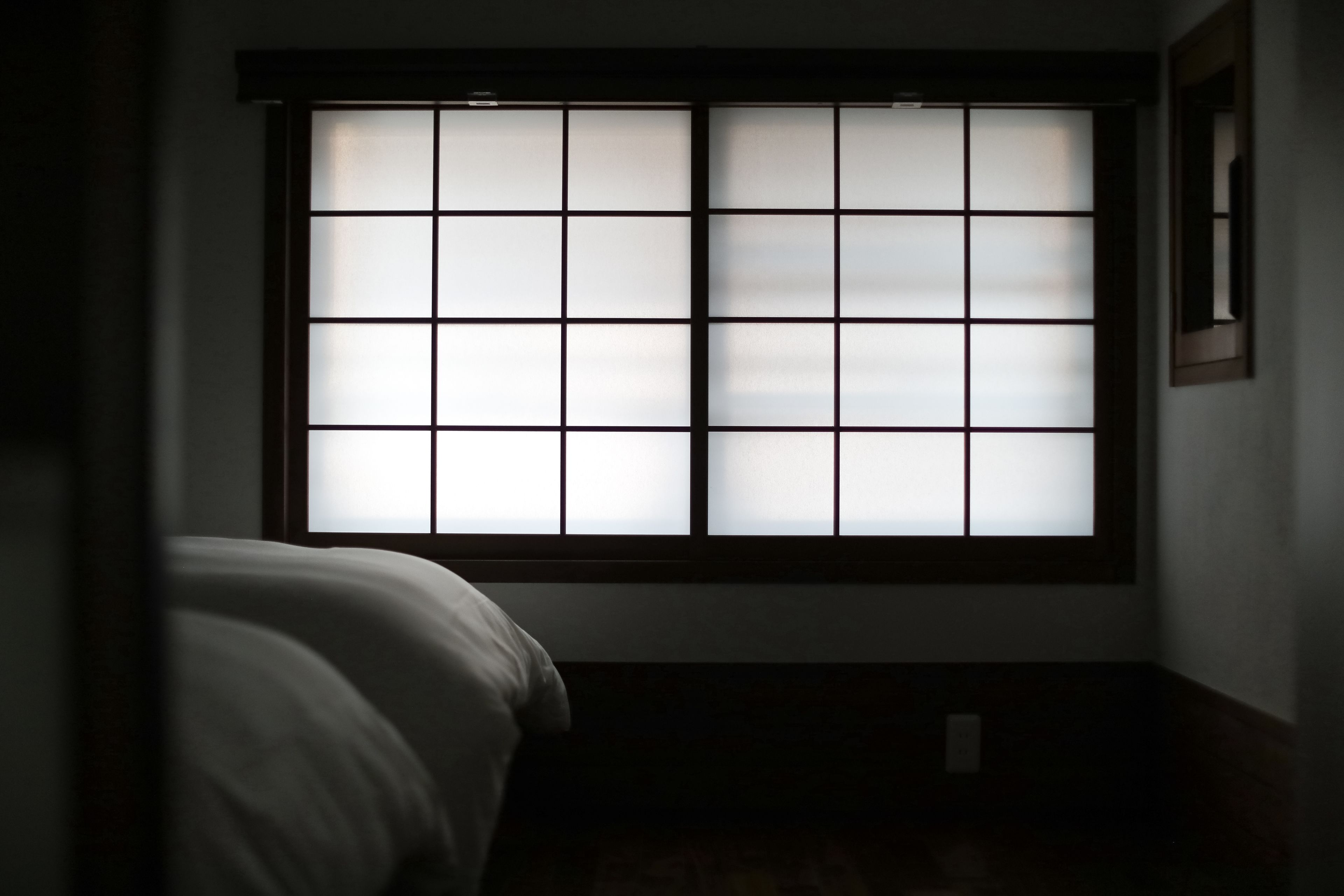 A room with a large window featuring a grid pattern, a bed, and a wall-mounted picture frame.