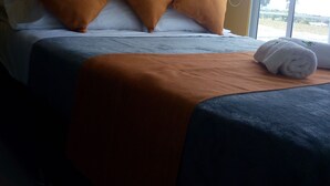A hotel room with a bed, three brown pillows, a white towel, and artwork on the wall. - Guaduales del café 304 (Montenegro)