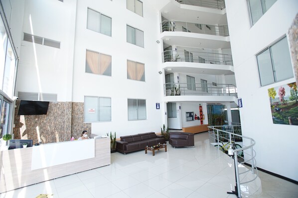 Un moderno vestíbulo de hotel con una recepción, área de estar y una escalera que conduce a los pisos superiores.