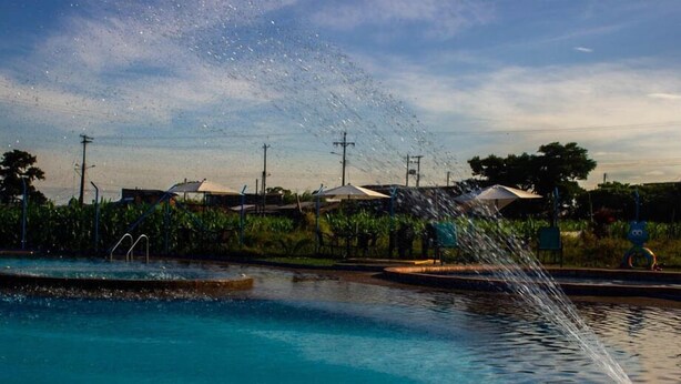 A swimming pool with water jets spraying upwards, surrounded by greenery and buildings in the background. - Guaduales del café 304 (Montenegro)