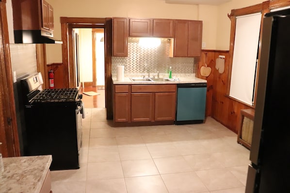 A compact kitchen with wooden cabinets, a black stove, a blue dishwasher, and a tiled backsplash. - COZY HOME- Located on a quiet Worthy Street with a home in its own compound. (Springfield)