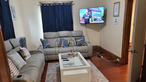 A living room with a beige sectional sofa, a glass coffee table, and a flat-screen TV mounted on the wall. - COZY HOME- Located on a quiet Worthy Street with a home in its own compound. (Springfield)