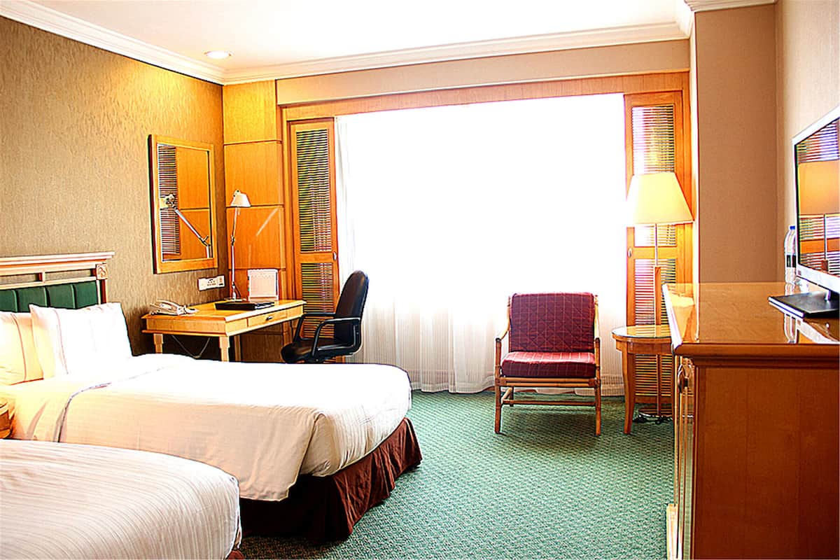 Una habitación de hotel con dos camas, un escritorio con lámpara, una silla y televisión.