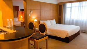 Una habitación de hotel con una cama, un escritorio con sillas, una lámpara y un ventanal con cortinas.