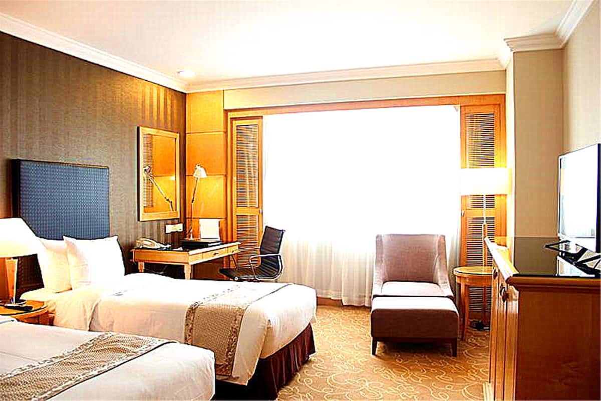 Una habitación de hotel con dos camas, un escritorio, una silla, un televisor y un ventanal grande.