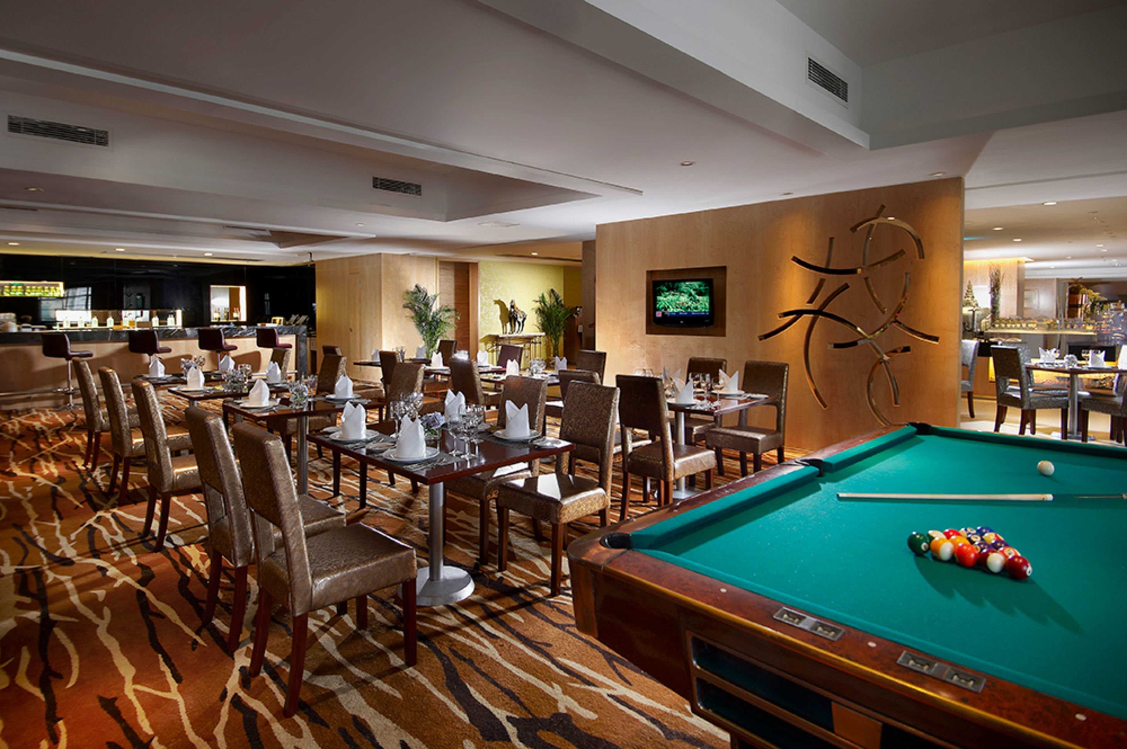 Een hotel lobby met een pooltafel, een eetgedeelte met tafels en stoelen, en een bar.