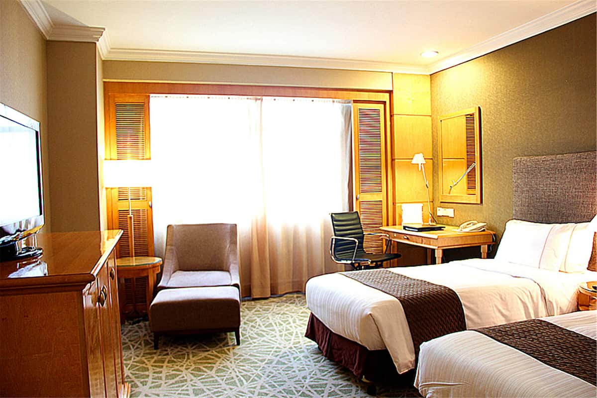Habitación de hotel con dos camas, un escritorio, una silla, un televisor y una ventana con cortinas.