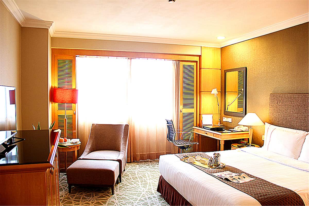 Habitación de hotel con cama, escritorio, silla, televisor y ventana con cortinas.