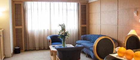 A hotel room with a large window, a sofa, a chair, a small table, and a lamp.