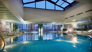 Una piscina interior con tragaluces, sillones de descanso y plantas en macetas.