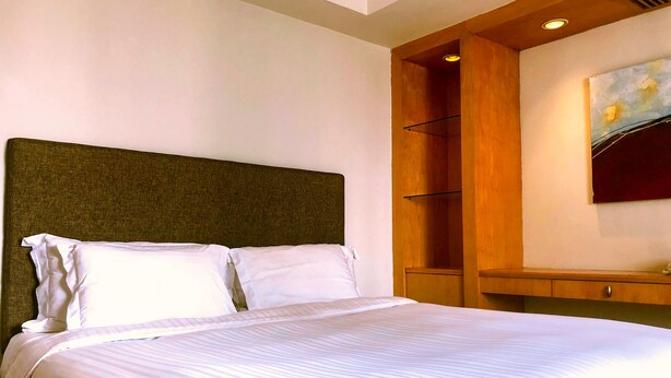 A hotel room with a large bed, a wooden headboard, a built-in shelf, and a painting on the wall. - Grand Park Wuxi (Wuxi)