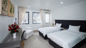 A hotel room with two beds, a desk with a vase of flowers, a white sofa, and artwork on the wall. - Smart Home Group (Ho Chi Minh City)