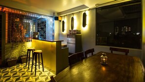 A modern kitchen with a bar area, a dining table with stools, and a city view through large windows. - Smart Home Group (Ho Chi Minh City)