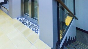 A modern elevator with a glass door, a metal control panel with a red 'M' button, and a wooden handrail. - Smart Home Group (Ho Chi Minh City)
