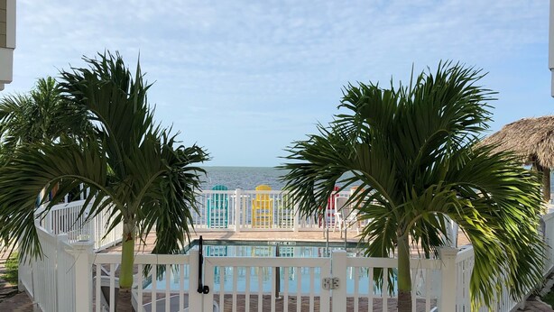 A pool area with a white fence, palm trees, and a view of the ocean.