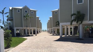 A paved walkway leading to a row of beige buildings with a covered entrance and palm trees.