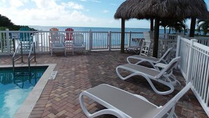 A poolside area with lounge chairs, a thatched umbrella, and a view of the ocean.