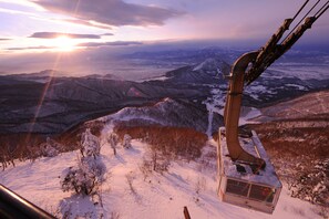 A cable car chair suspended over a snowy landscape with distant mountains and a sunset.