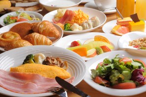 A breakfast buffet with various dishes including croissants, eggs, fruits, and vegetables.