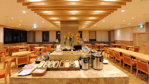 Un comedor amplio con varias mesas y sillas, un sistema de buffet con diversos alimentos, y un diseño de techo moderno.