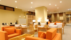 Un moderno vestíbulo de hotel con sofás naranjas, sillas de madera y un mostrador de recepción.