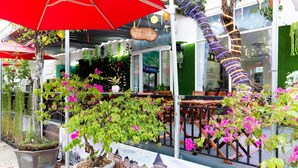 An outdoor seating area with tables and chairs, surrounded by potted plants and a large red umbrella. - Zone 5 Boutique Hotel (Da Nang)